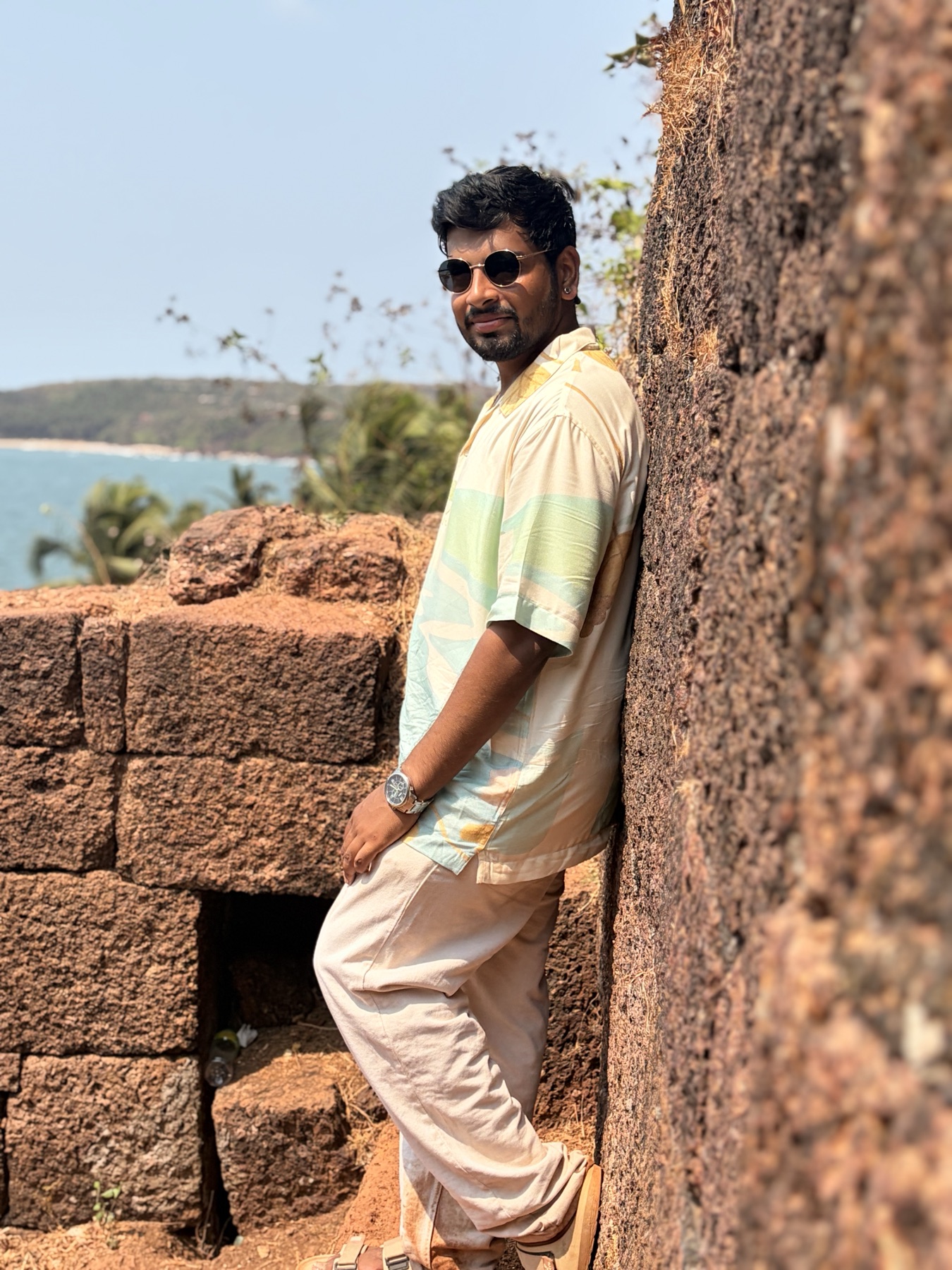 Ankit standing by a coastal fort wall in sunglasses