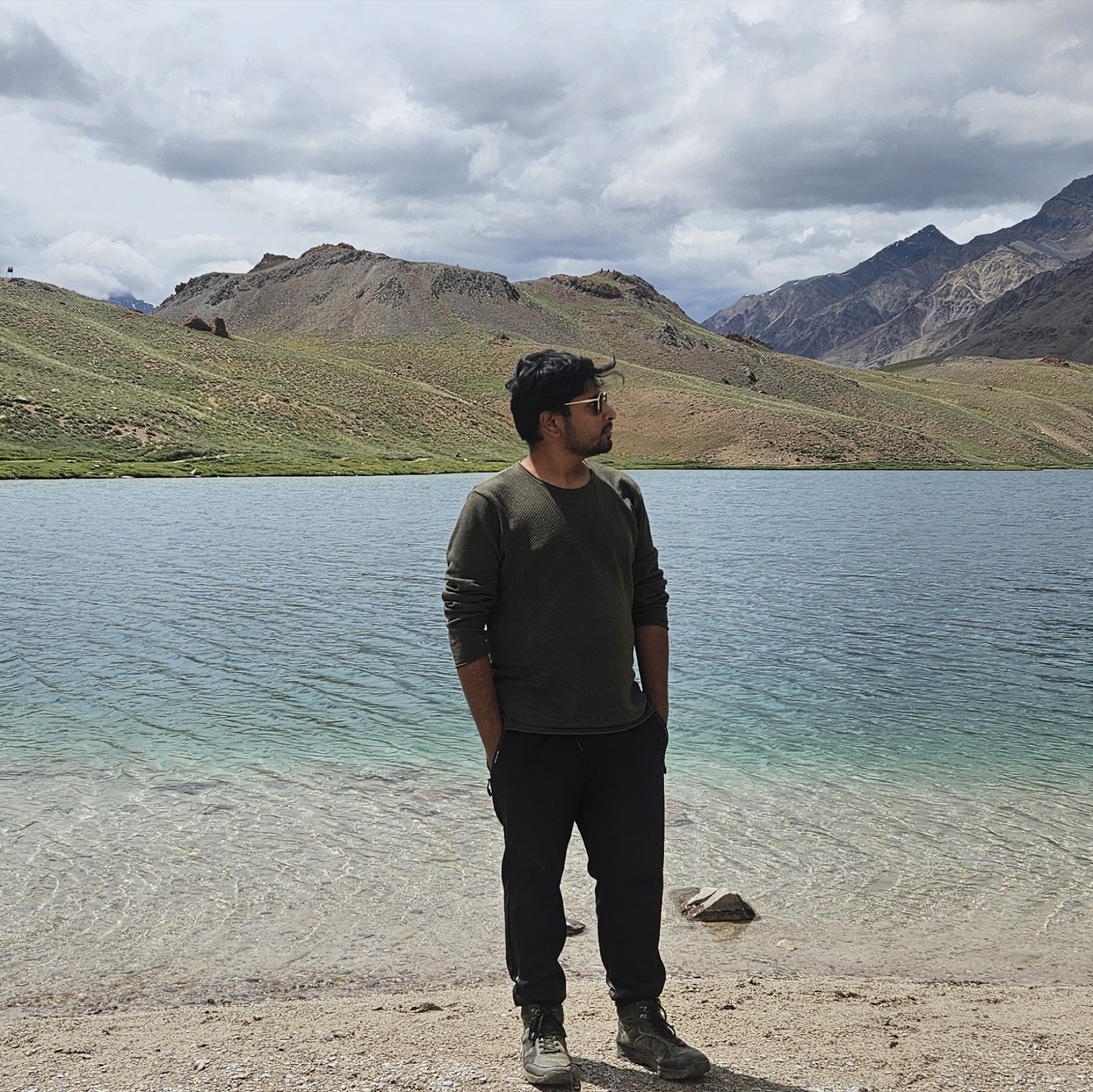 Ankit beside a mountain lake under dramatic clouds